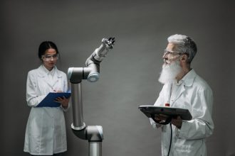 Dois pesquisadores analisam um braço robótico em um laboratório de inovação tecnológica.