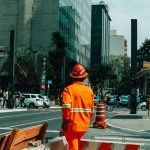 Trabalhador da construção civil em uma movimentada rua de São Paulo, cercado por edifícios e circulação urbana.