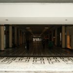 Corredor amplo de um shopping center moderno, com pessoas caminhando entre as lojas.