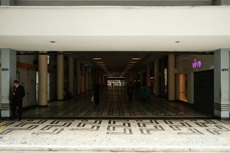 Corredor amplo de um shopping center moderno, com pessoas caminhando entre as lojas.