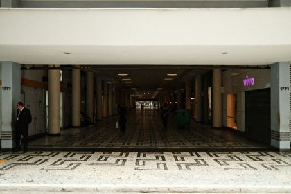 Corredor amplo de um shopping center moderno, com pessoas caminhando entre as lojas.