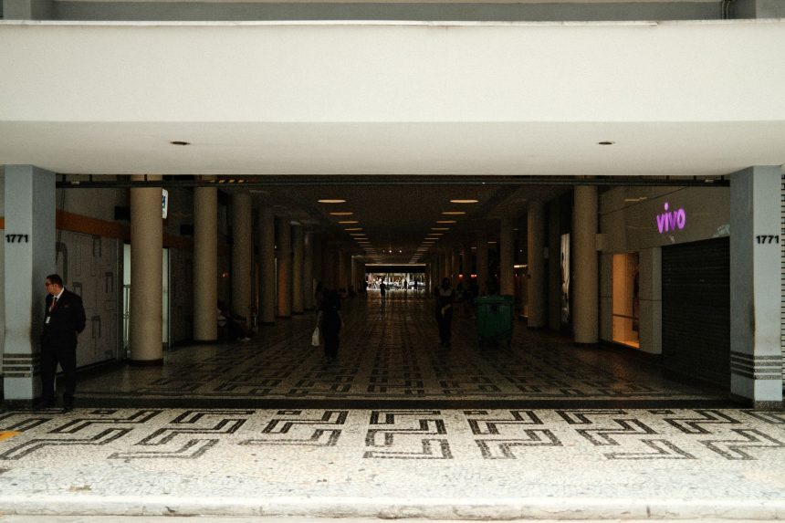 Corredor amplo de um shopping center moderno, com pessoas caminhando entre as lojas.